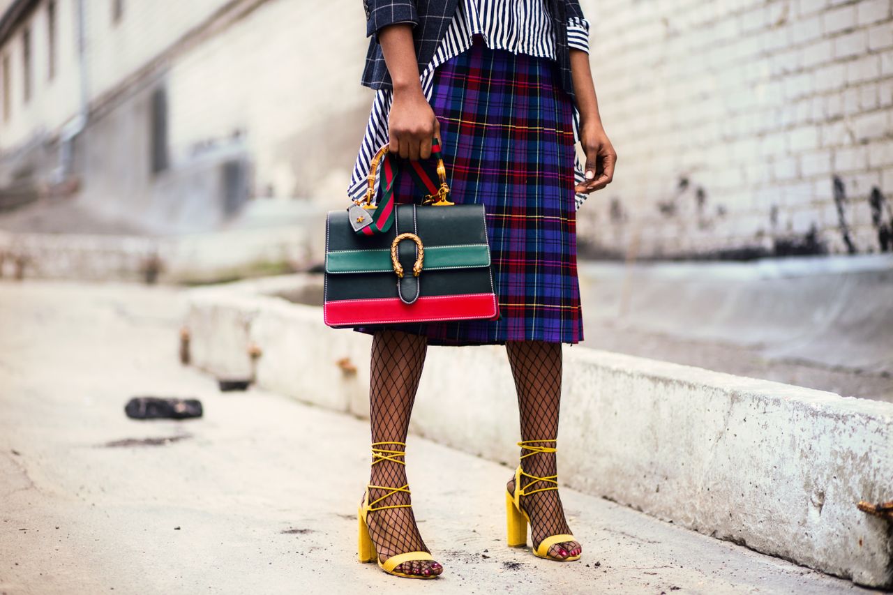 about-02 Fashion-forward outfit with plaid skirt and colorful handbag in urban setting.